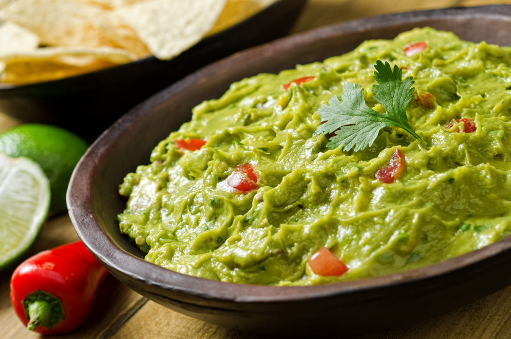A bowl of creamy guacamole dip with peppers, tomato, cilantro, and lime.