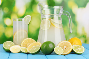 Citrus lemonade in pitcher and glass of citrus around on natural wooden table on blue background