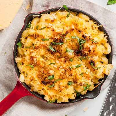 Mac and cheese, american style macaroni pasta with cheesy sauce and crunchy breadcrumbs topping, in portioned pan, white marble table, copy space top view